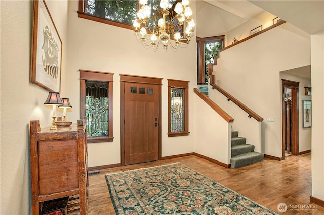 foyer featuring stairway, a high ceiling, an inviting chandelier, wood finished floors, and baseboards