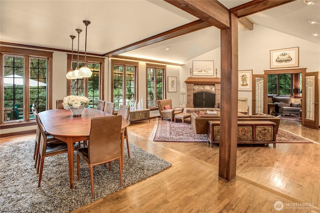 dining room featuring a healthy amount of sunlight, a fireplace, beamed ceiling, and wood finished floors