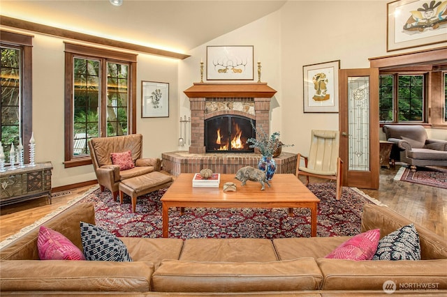 living area with a wealth of natural light, vaulted ceiling, a fireplace, and wood finished floors