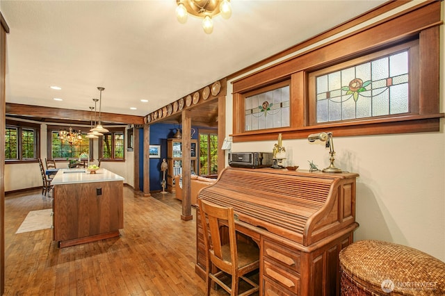 kitchen with light wood finished floors, a kitchen island, decorative light fixtures, light countertops, and a notable chandelier