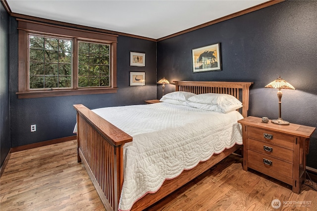 bedroom featuring a textured wall, light wood finished floors, and baseboards