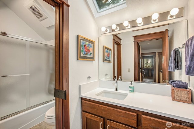 bathroom featuring toilet, vanity, visible vents, combined bath / shower with glass door, and lofted ceiling with skylight