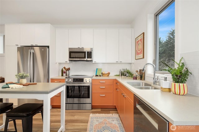 kitchen with stainless steel appliances, a sink, white cabinets, light countertops, and light wood finished floors