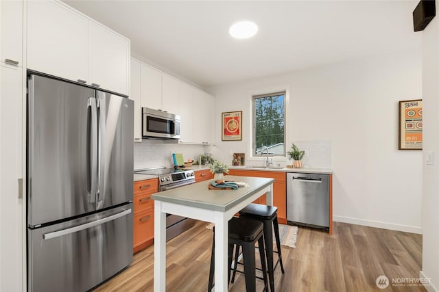 kitchen with stainless steel appliances, a sink, white cabinetry, light countertops, and backsplash