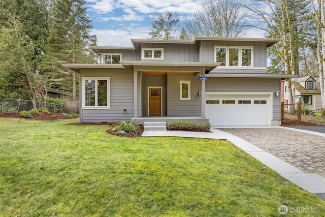 prairie-style house with an attached garage, board and batten siding, a front lawn, and decorative driveway