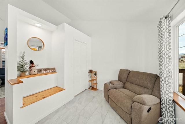 sitting room featuring lofted ceiling, marble finish floor, and baseboards