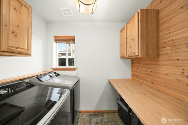 laundry area featuring washer and clothes dryer, visible vents, cabinet space, stone finish floor, and baseboards