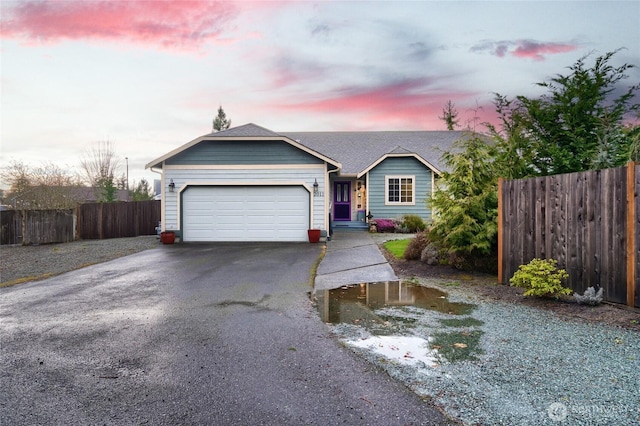 ranch-style house featuring an attached garage, a shingled roof, fence, and aphalt driveway