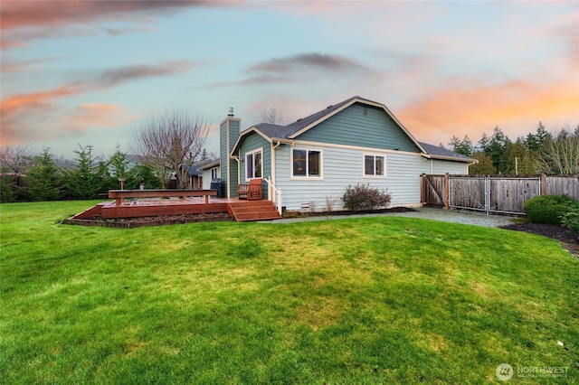 back of house at dusk with a deck, a yard, a chimney, and fence