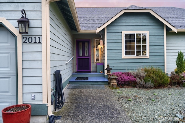 exterior entry at dusk featuring an attached garage and a shingled roof