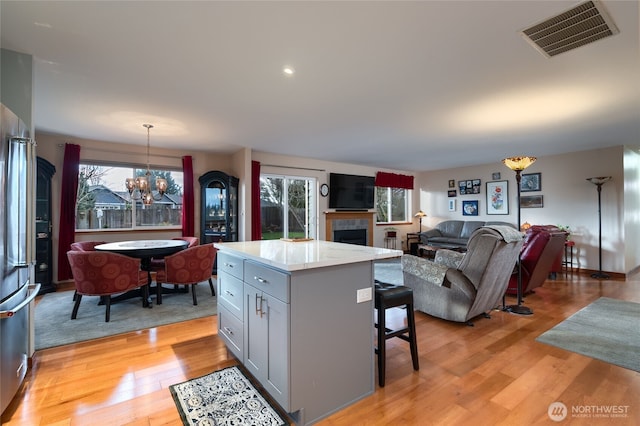 kitchen featuring a chandelier, a breakfast bar, a fireplace, visible vents, and light wood finished floors