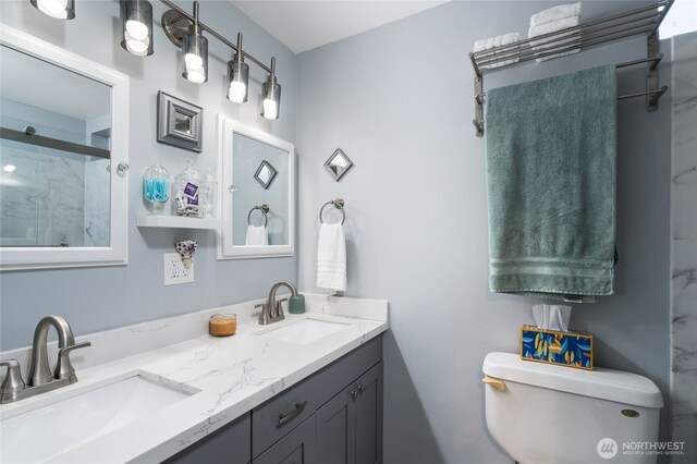 full bath with toilet, a shower stall, double vanity, and a sink