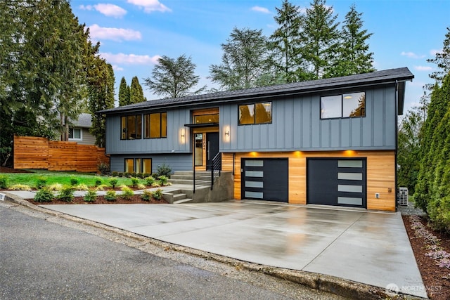 raised ranch with a garage, board and batten siding, fence, and concrete driveway