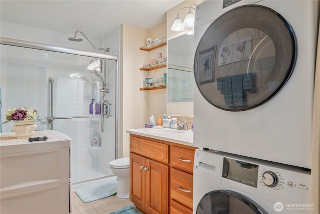 bathroom with tile patterned flooring, toilet, vanity, a shower stall, and stacked washer and clothes dryer