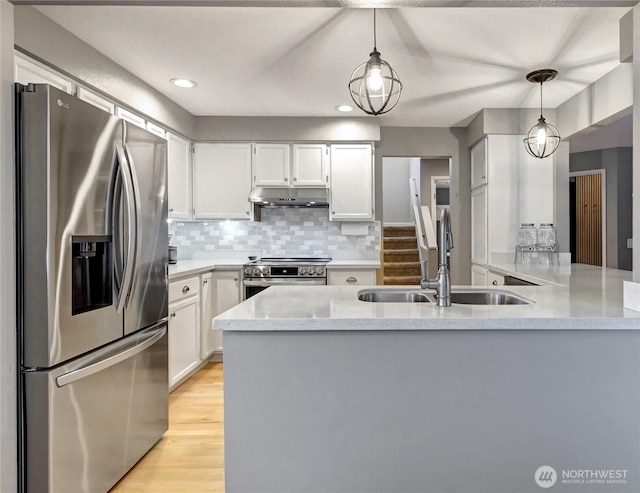 kitchen with under cabinet range hood, a peninsula, a sink, appliances with stainless steel finishes, and backsplash