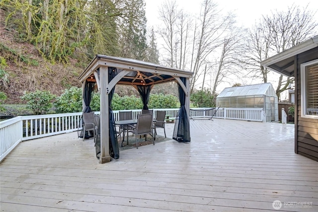 wooden deck featuring a gazebo, outdoor dining space, an outdoor structure, and an exterior structure