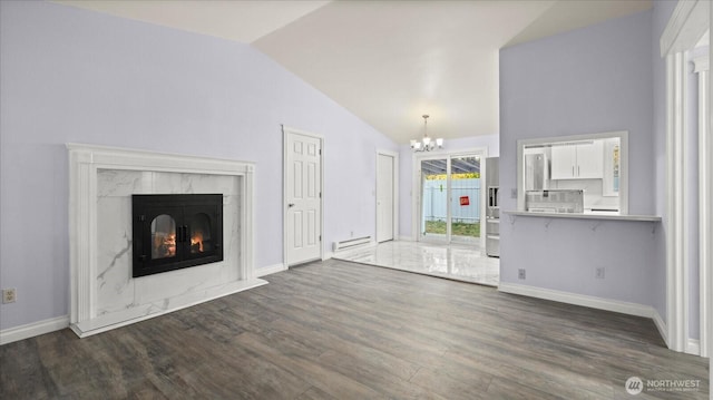 unfurnished living room featuring a notable chandelier, a baseboard heating unit, wood finished floors, a high end fireplace, and vaulted ceiling