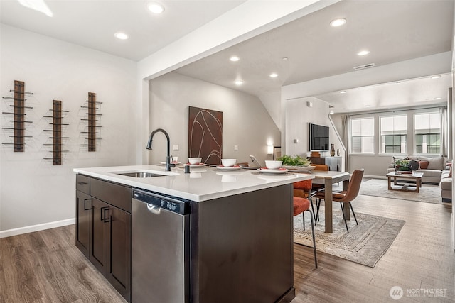 kitchen with a center island with sink, light countertops, open floor plan, a sink, and dishwasher