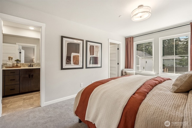 bedroom with light carpet, baseboards, a sink, and ensuite bathroom