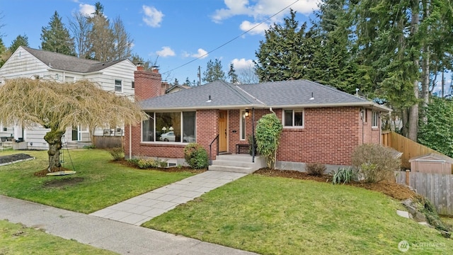 ranch-style home with brick siding, fence, a front lawn, and roof with shingles