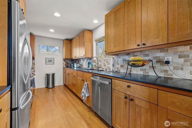 kitchen with a sink, appliances with stainless steel finishes, brown cabinets, light wood finished floors, and dark countertops