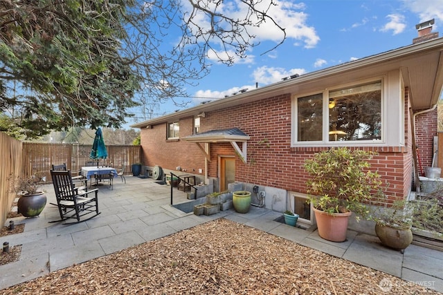 exterior space featuring a patio, a fenced backyard, brick siding, outdoor dining space, and a chimney