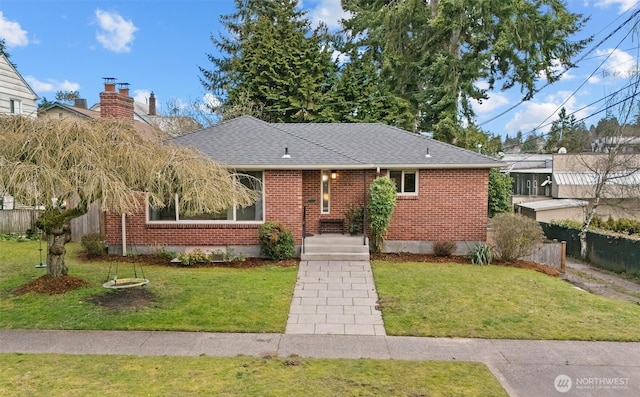 ranch-style home with roof with shingles, brick siding, a front lawn, and fence