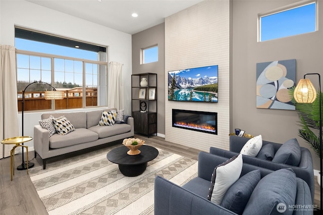 living area featuring baseboards, a towering ceiling, wood finished floors, a fireplace, and recessed lighting