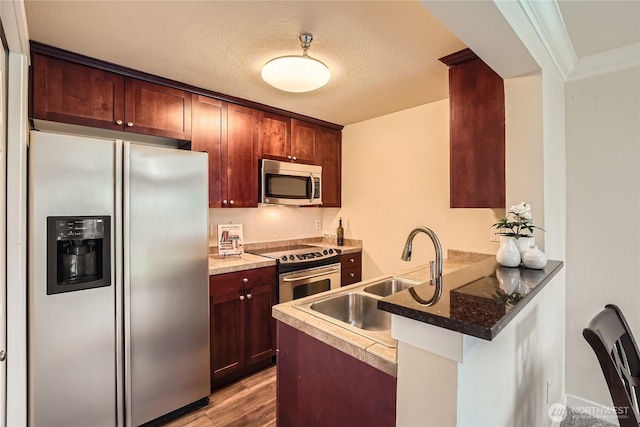 kitchen featuring a peninsula, wood finished floors, a textured ceiling, stainless steel appliances, and a sink