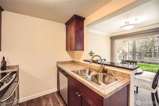 kitchen featuring baseboards, dark wood finished floors, appliances with stainless steel finishes, a peninsula, and a sink