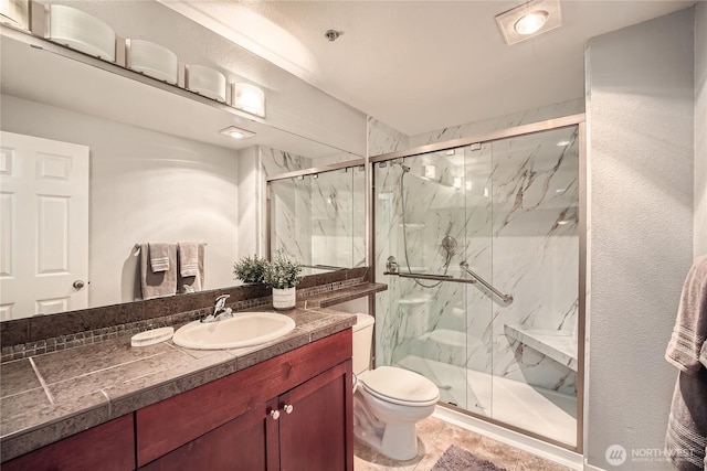 full bathroom with a marble finish shower, toilet, and vanity