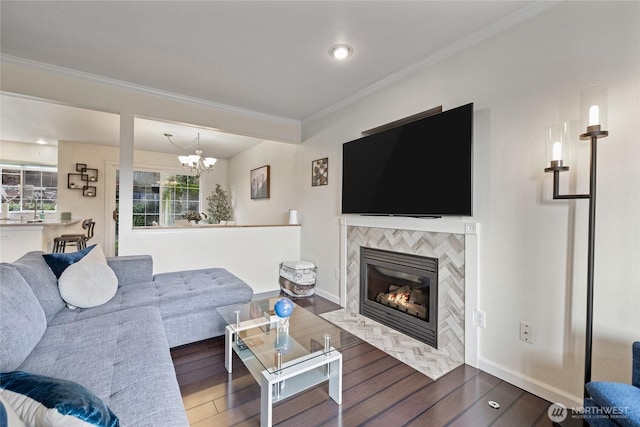 living room featuring baseboards, a tiled fireplace, wood-type flooring, crown molding, and a chandelier