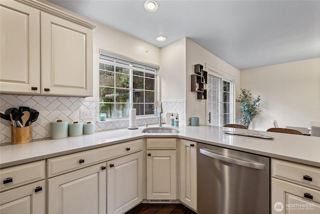 kitchen with light countertops, stainless steel dishwasher, cream cabinets, and a sink