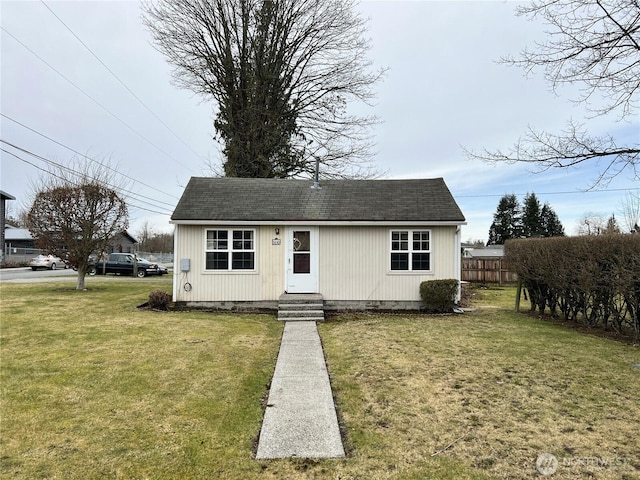 view of front of home with entry steps, roof with shingles, fence, and a front yard