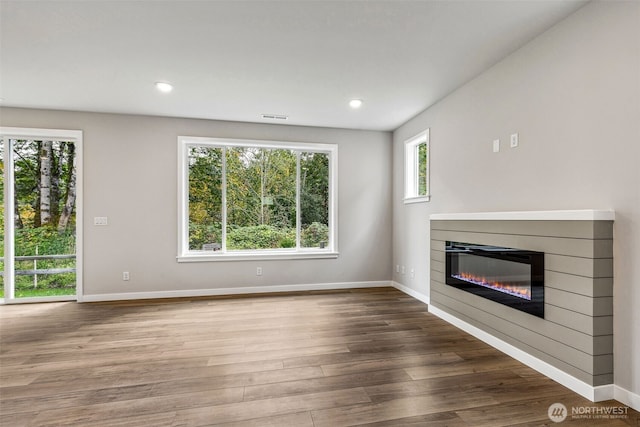 unfurnished living room featuring baseboards, visible vents, wood finished floors, and a glass covered fireplace