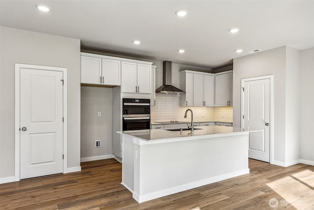 kitchen with double wall oven, wall chimney range hood, backsplash, and wood finished floors