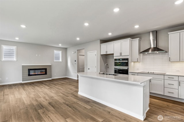 kitchen featuring black electric cooktop, double wall oven, a sink, dark wood-style floors, and wall chimney exhaust hood