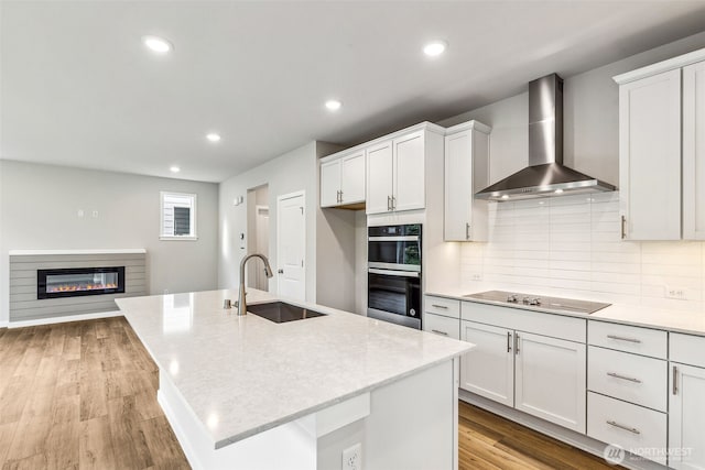 kitchen with backsplash, stainless steel double oven, a sink, wall chimney exhaust hood, and black electric cooktop