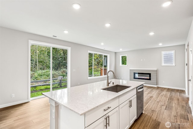 kitchen with a glass covered fireplace, a sink, light wood-type flooring, stainless steel dishwasher, and recessed lighting