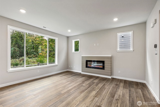 unfurnished living room with recessed lighting, baseboards, wood finished floors, and a glass covered fireplace