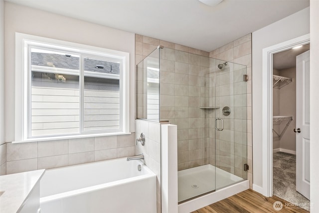 bathroom featuring a stall shower, baseboards, wood finished floors, a walk in closet, and a bath