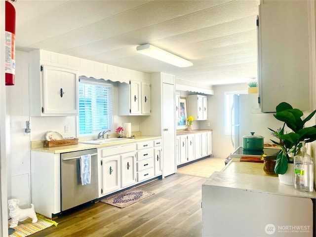 kitchen featuring light wood-style flooring, a sink, white cabinets, light countertops, and dishwasher