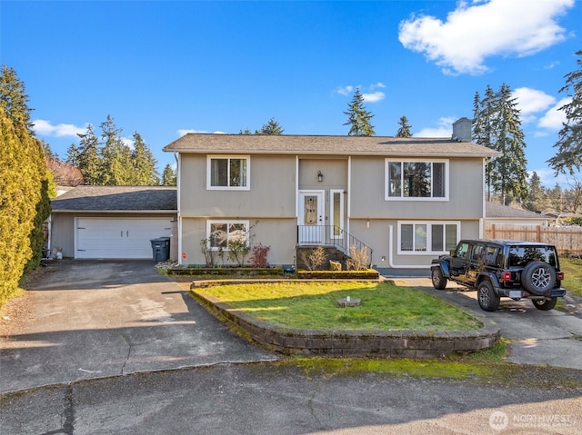 raised ranch featuring a garage, concrete driveway, a chimney, fence, and a front lawn