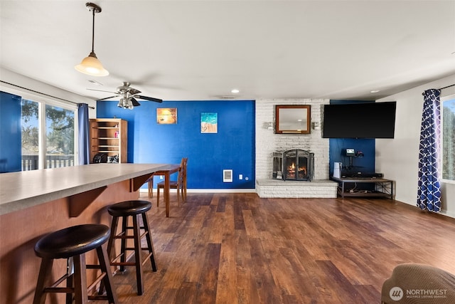 interior space with dark wood-style floors, a brick fireplace, ceiling fan, and baseboards