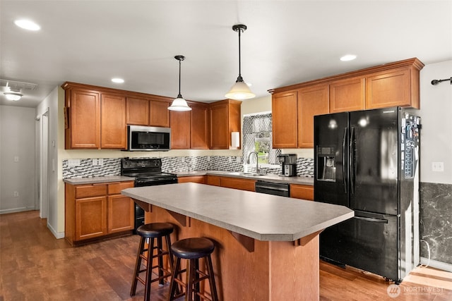 kitchen featuring black appliances, dark wood-type flooring, brown cabinetry, and a sink