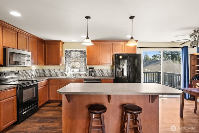 kitchen with dark wood-style flooring, a sink, a center island, black appliances, and a kitchen bar