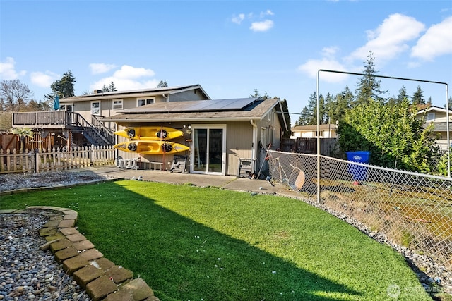 rear view of house featuring a fenced backyard, roof mounted solar panels, a lawn, and a patio