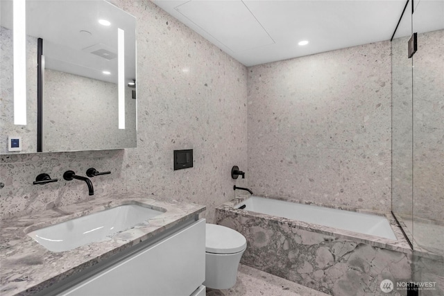 bathroom featuring toilet, a tub with marble appearance, recessed lighting, tile walls, and vanity