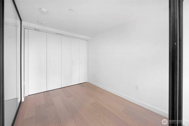 unfurnished bedroom featuring wood finished floors, baseboards, and a closet