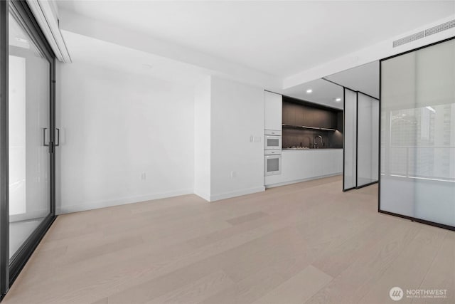 interior space with light wood finished floors, visible vents, baseboards, and a sink